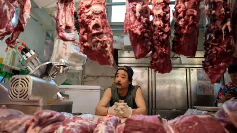 Getty Images Butcher looks at meat hanging in a shop in China
