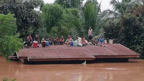 EPA Lao villagers are stranded on the roof of a house after a dam collapsed in Attapeu province, Laos, 24 July 2018