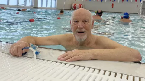 BBC Bob Young at the shallow end of the pool with his arms in the air, smiling and wearing goggles.