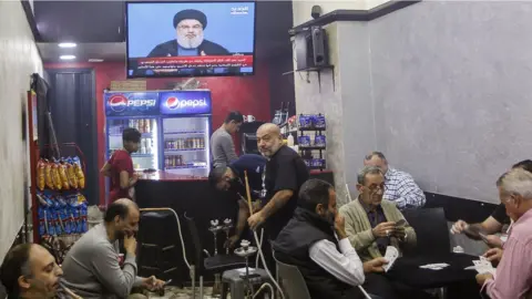 EPA Lebanese men play cards and smoke shishas while listening to a speech by Hezbollah leader Hassan Nasrallah on TV at a coffee shop in Beirut, Lebanon (5 November 2017)