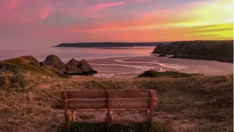 Sarah Shaw Looking towards an empty bench, the perfect seat to enjoy the sky's rich colours at sunset