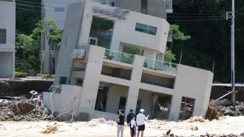 EPA People stand in front of a collapsed building on a beach in Pohang