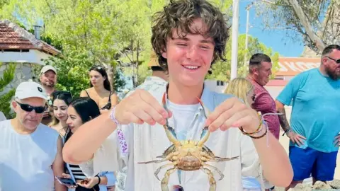 Family photo Harvey Owen in the middle of a group of people holding a crab by the pincers and smiling