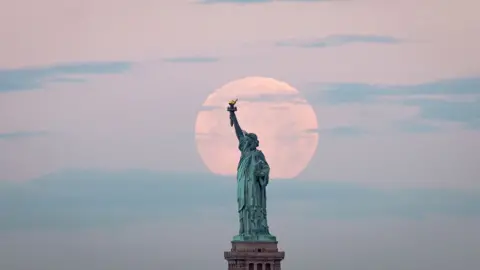 AFP May"s full Moon, known as the Full Flower Moon and is the last supermoon of the year, sets behind the Statue of Liberty in New York City