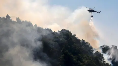 Getty Images A helicopter drops water as firefighters work to extinguish a wild fire in Mount Dajti, east of capital Tirana, 4 August 2017