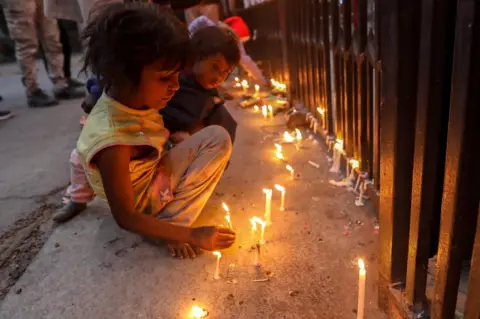 EPA Children light candles at the entrance gate of the Sacred Heart Cathedral in Delhi, India. Photo: 24 December 2020