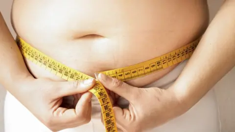 Getty Images A teen measuring their waistline