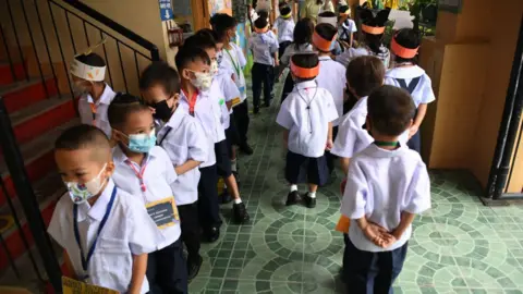 Getty Images Teachers watch their students walk along a corridor after a short break at the start of classes at a school in Quezon City