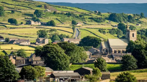 Getty Images A view of a traditional village in the Yorkshire Dales, with a grey stone church and a number of houses also of stone and farm buildings in the foreground