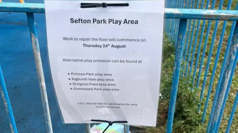 Handout A laminated piece of white A4 paper fixed to a blue metal fence. It reads: "Sefton Park Play Area. Work to repair the floor will commence on Thursday 24th August. Alternative play provision can be found at Princes Park, Aigburth Vale, St Agnes Field, Greenbank Park. LCC would like to apologise for any inconvenience."