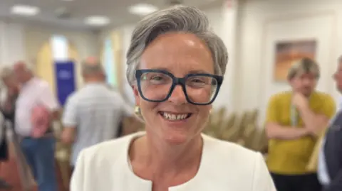 Lady wearing a white jacket and big glasses smiling at the camera