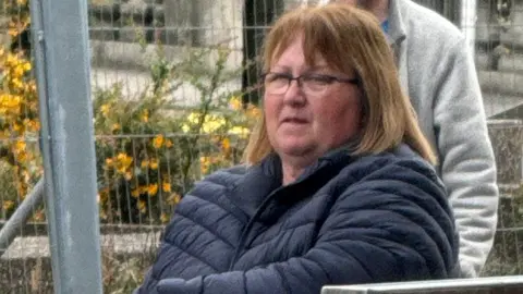 Yvonne Keenan pictured outside court. She has shoulder-length brown hair and is wearing glasses and a blue puffa jacket