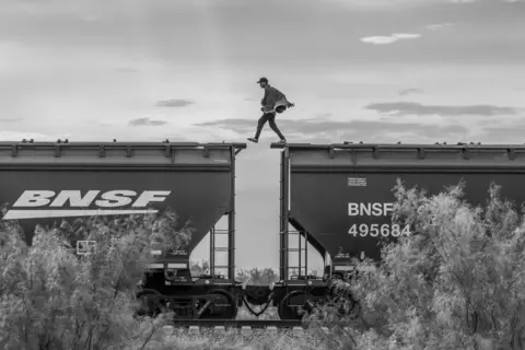 Alejandro Cegarra for The New York Times A migrant walks atop a freight train known, Piedras Negras, Mexico, 8 October 2023