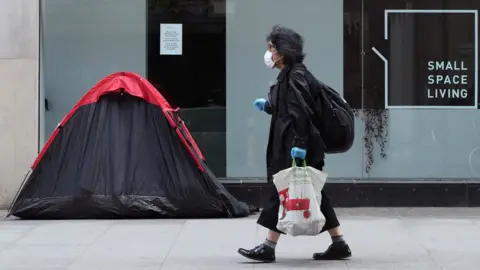 PA Media A woman walking past a homeless person's tent erected outside a furniture store