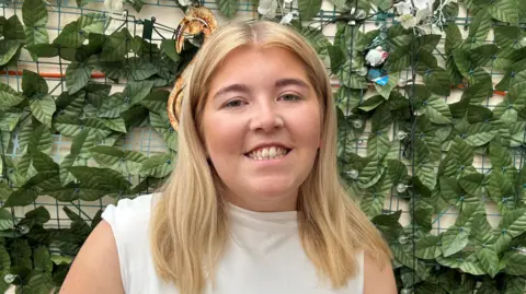 BBC A girl in a white top smiling at the camera 