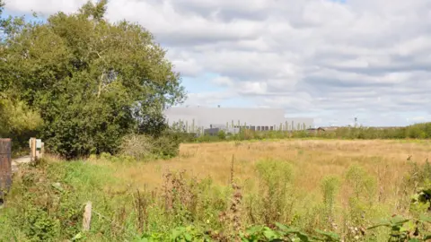 A visual representation of the Energy Recovery Facility at Chapel Gate Eco Park - a large grey boxy building - looking from across a field.