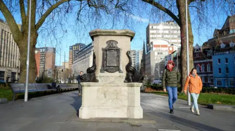 The plinth which used to have the statue of Edward Colston standing on top of it is pictured on a bright day in the centre of Bristol with two people walking past it