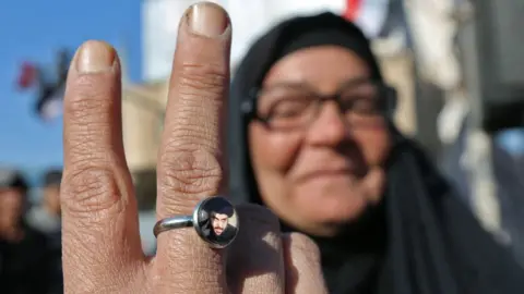 AFP An Iraqi anti-government protester in Baghdad shows a ring bearing a portrait of Moqtada al-Sadr (20 November 2019)