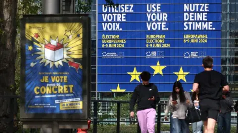 FREDERICK FLORIN/AFP Voetgangers lopen langs een gigantische poster die de komende Europese verkiezingen aankondigt, gepleisterd op de gevel van het gebouw van het Europees Parlement in Straatsburg, Oost-Frankrijk, op 10 april 2024. De verkiezingen voor het Europees Parlement zijn gepland voor 6 juni. tot 9.2024.