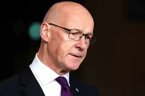 PA Media A bald headed man with glasses, wearing a purple tie, white shirt and dark suit