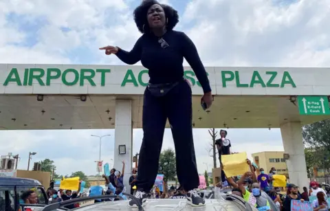 Reuters A demonstrator stands atop a vehicle and shouts slogans as others carry banners while blocking a road leading to the airport, during a protest over alleged police brutality, in Lagos, Nigeria October 12, 2020.