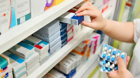 Getty Images A pharmacy worker lifts a box of tablets from a shelf medicine cabinet