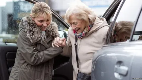 Getty Images Young lady helping older woman out of a car