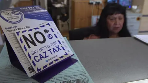 Cindy Holmes sat behind a desk with a No CAZ tax sign on it