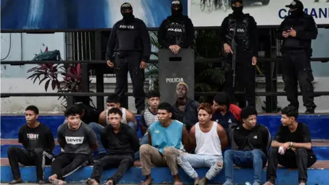Reuters Police officers stand behind a group of detainees in Guayaquil, Ecuador on 10 January 2024.