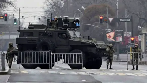 Reuters Kazakh service members stand guard at a checkpoint following the protests triggered by fuel price increase in Almaty on 7 January