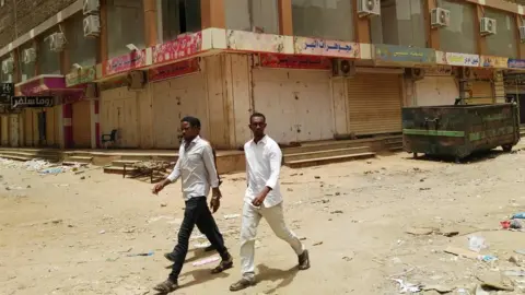 AFP A group of men walk past a row of closed up shops in Khartoum's twin city, Omdurman