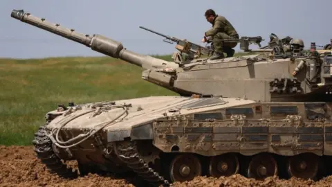 An Israeli soldier unloads a weapon on top of a tank near Israel"s border with Gaza, 30 March 2024