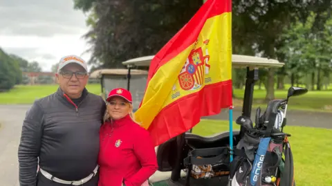 A man and a women stand beside a golf buggy 