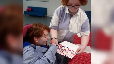 A volunteer helping a disabled child to paint.