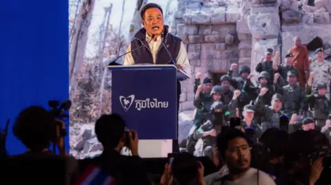 Jonathan Head/ BBC Anutin speaking at a rally in front of a photo showing Thai soldiers photographed during the border conflict with Cambodia.