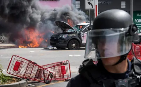 Getty Images Police vehicles burn after being set on fire by demonstrators in the Fairfax District of Los Angeles as they protest the death of George Floyd, 30 May 2020