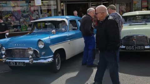 Rob Coombes Three men standing next to a blue 1950s Ford Consols