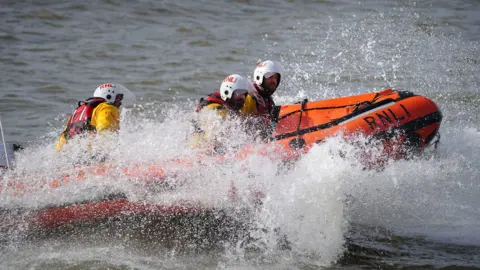 PA Media Four crew members on an RNLI lifeboat in the water with water splashing up