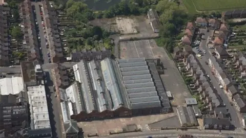 West Northamptonshire Council Aerial view showing a line of bus garages with grey roofs, surrounded by houses and trees