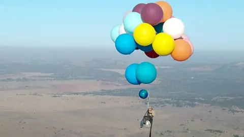 Reuters Tom Morgan, from Bristol-based company The Adventurists, flies in a chair with large party balloons tied to it near Johannesburg, South Africa 20/10/2017