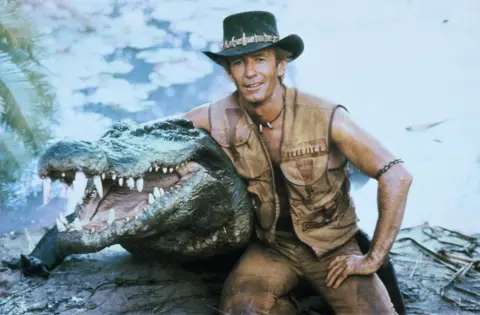 Shutterstock Paul Hogan dengan buaya palsu di lokasi syuting Crocodile Dundee. Hanya sekali pakai, gambar dibayar per penggunaan.