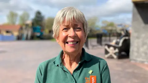 A woman stands in front of a ride at Crealy Theme Park in Devon, she is wearing a green t shirt. 