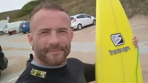 Pip Holmes Pip Holmes standing with his surfboard