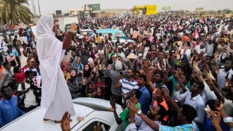 AFP/Getty Images Protesters in Khartoum hold up their phones to film fellow protester Alla Salah who stands on a car dressed in a white headscarf and skirt