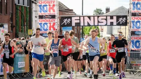 Runners taking part in the Chorley 10k with crowds lining the street to cheer them on. The race starts and finishes on Market Street with a black and white sign