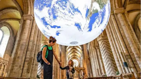 Durham Cathedral A mother and child pause under the illuminated earth suspended from the nave