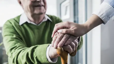 Getty Images A woman placing her hand on those of an elderly man