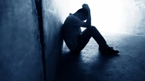 Getty Images Man sat against a wall