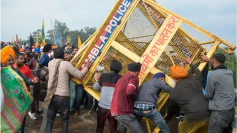 Getty Images Farmers remove a police barricade in Haryana in protest