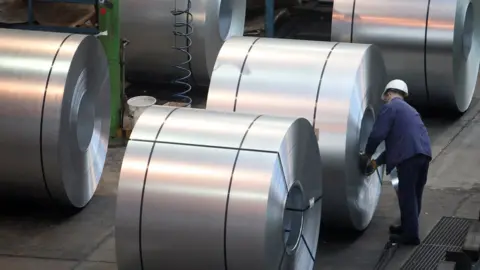 Getty Images A worker inspects rolls of steel at a factory